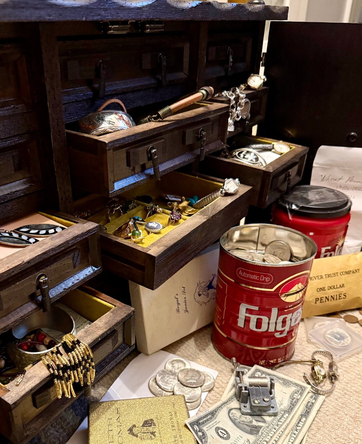 An open wooden jewelry trunk beside coffee cans and coins